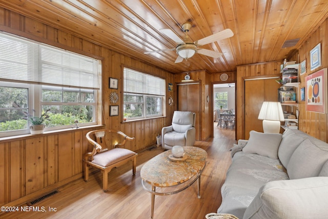 living room featuring ceiling fan, a healthy amount of sunlight, light wood-type flooring, and wood walls