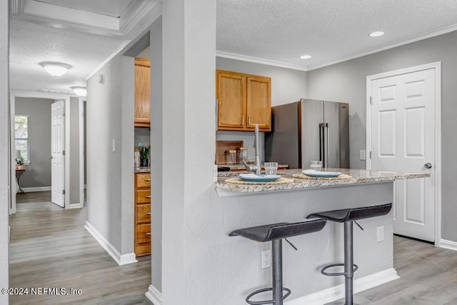 kitchen featuring ornamental molding, stainless steel fridge, light wood-type flooring, and a breakfast bar