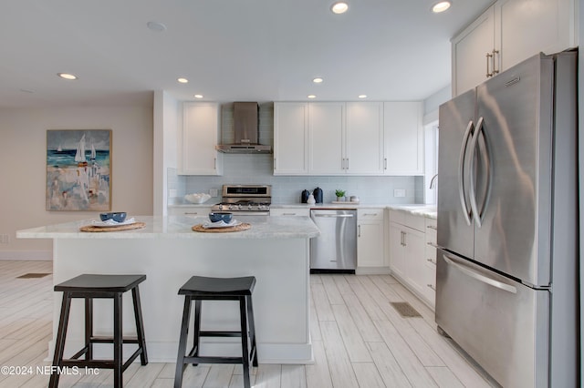 kitchen featuring appliances with stainless steel finishes, a kitchen island, white cabinetry, and wall chimney exhaust hood