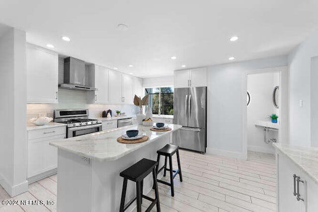 kitchen featuring white cabinetry, wall chimney exhaust hood, stainless steel appliances, and light stone counters