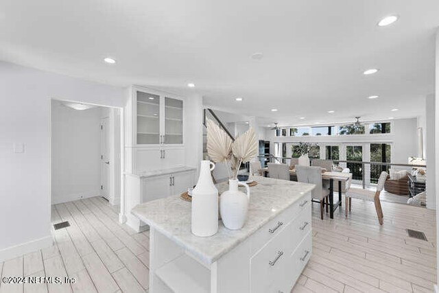 kitchen with light wood-type flooring, white cabinetry, a kitchen island, and light stone counters