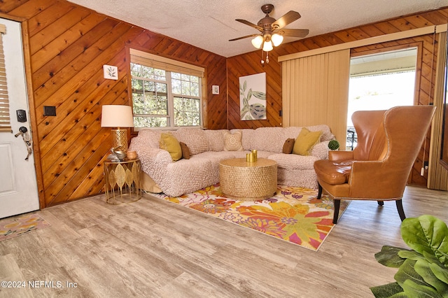 living room featuring light wood-type flooring, wooden walls, and a textured ceiling