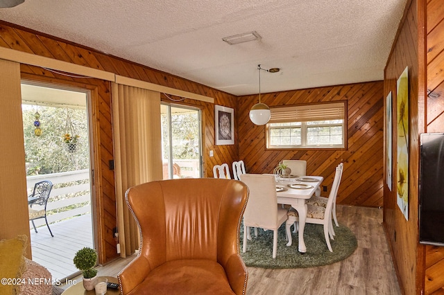 dining area with wooden walls, wood-type flooring, and a textured ceiling