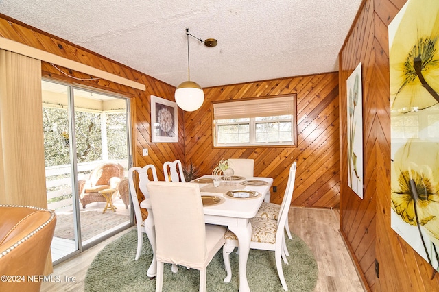 dining space featuring wooden walls, light hardwood / wood-style flooring, and a textured ceiling