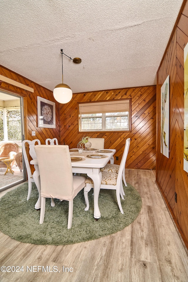 dining space with wood-type flooring, wooden walls, and a textured ceiling