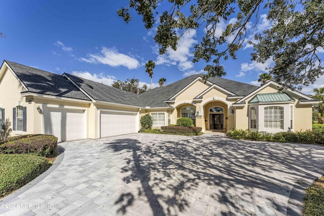 ranch-style home featuring an attached garage, stucco siding, and decorative driveway