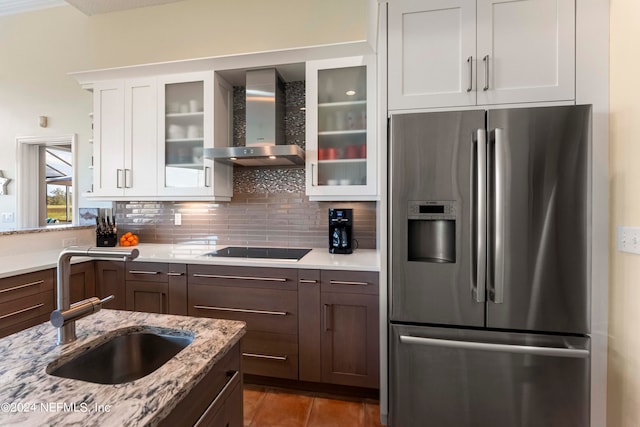 kitchen featuring white cabinets, stainless steel refrigerator with ice dispenser, wall chimney exhaust hood, light stone countertops, and black electric cooktop