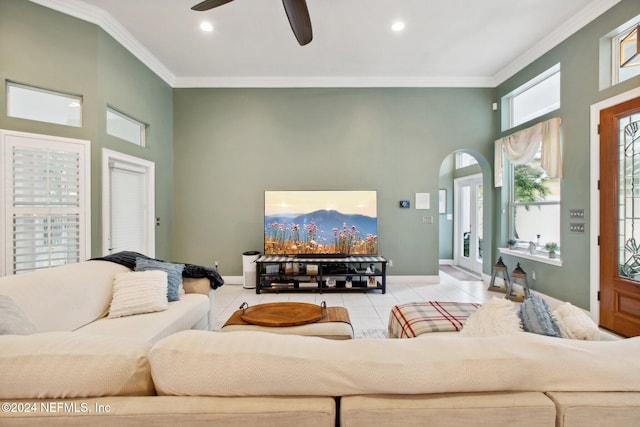 tiled living room with ceiling fan, crown molding, and a high ceiling