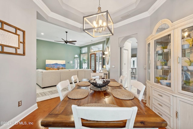 dining space featuring ceiling fan with notable chandelier, light wood-type flooring, a tray ceiling, and ornamental molding