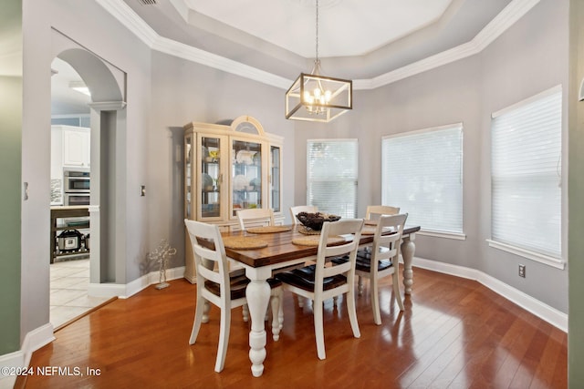 dining room with light hardwood / wood-style floors, a raised ceiling, ornamental molding, and a notable chandelier