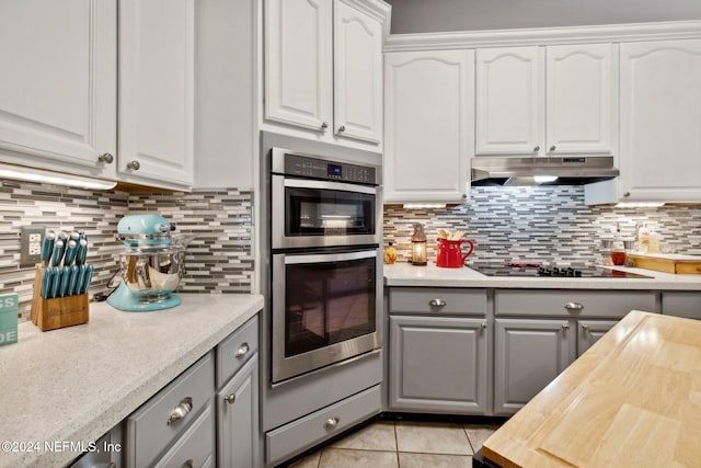 kitchen featuring backsplash, white cabinetry, light tile patterned floors, and stainless steel double oven