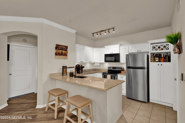 kitchen with appliances with stainless steel finishes, kitchen peninsula, white cabinetry, and light wood-type flooring