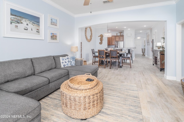 living room featuring ceiling fan, light wood-style floors, arched walkways, baseboards, and ornamental molding