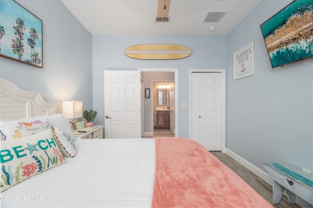bedroom featuring connected bathroom, baseboards, wood finished floors, visible vents, and a closet
