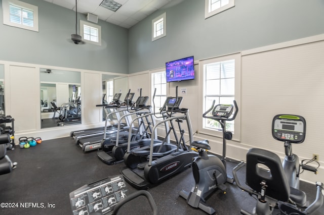 gym with a towering ceiling, a drop ceiling, and a healthy amount of sunlight