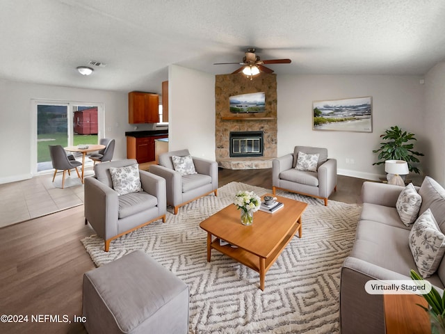 living room with a fireplace, a textured ceiling, light hardwood / wood-style floors, ceiling fan, and vaulted ceiling