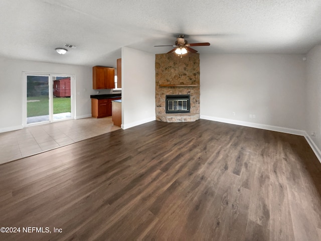 unfurnished living room featuring a stone fireplace, a textured ceiling, light wood-type flooring, and ceiling fan