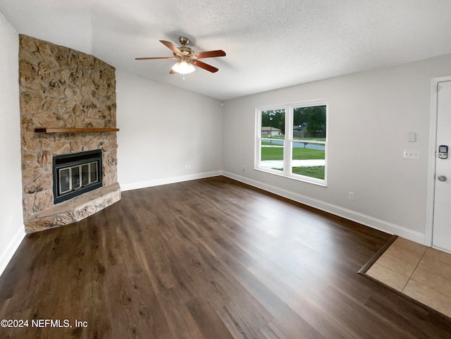 unfurnished living room featuring a stone fireplace, dark hardwood / wood-style floors, a textured ceiling, and ceiling fan