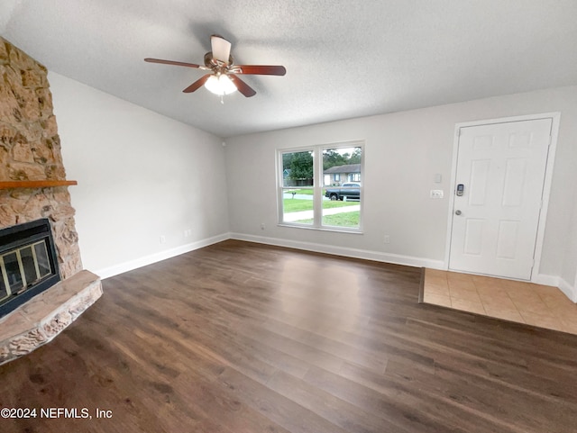 unfurnished living room with a stone fireplace, a textured ceiling, ceiling fan, and dark hardwood / wood-style flooring