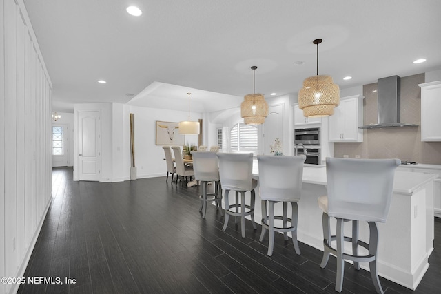 kitchen featuring wall chimney exhaust hood, dark hardwood / wood-style flooring, pendant lighting, a kitchen island with sink, and white cabinets