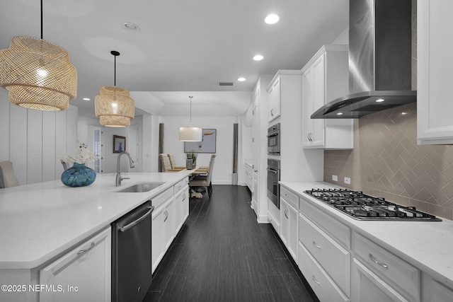 kitchen with wall chimney range hood, sink, white cabinetry, stainless steel appliances, and decorative light fixtures