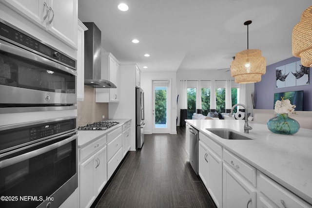 kitchen featuring wall chimney exhaust hood, sink, white cabinetry, hanging light fixtures, and stainless steel appliances