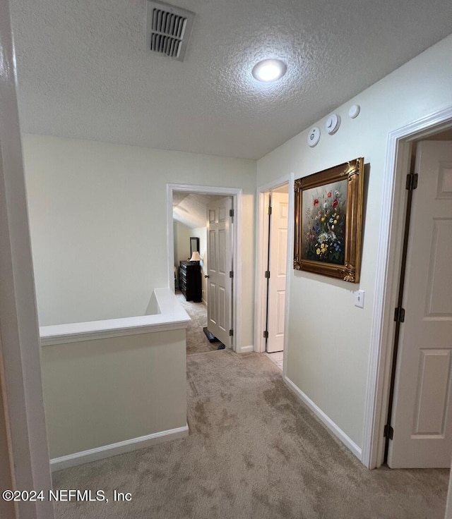 corridor with a textured ceiling and light colored carpet