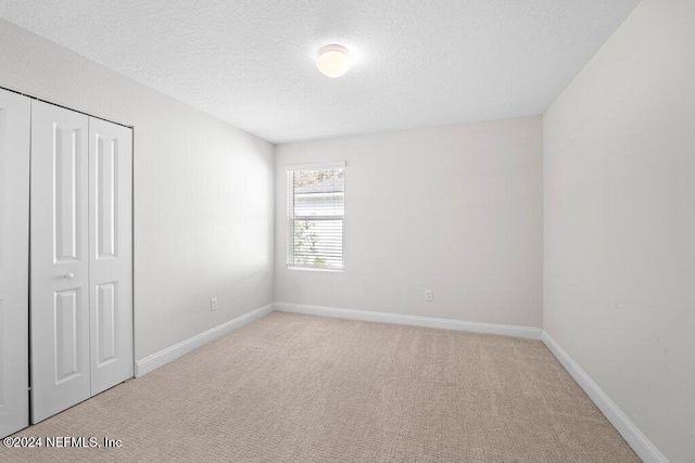 unfurnished bedroom featuring light carpet, a textured ceiling, and a closet