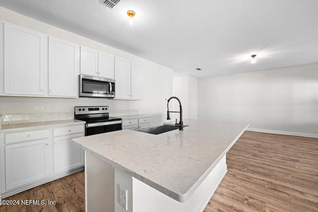 kitchen featuring appliances with stainless steel finishes, sink, white cabinets, light hardwood / wood-style flooring, and a kitchen island with sink