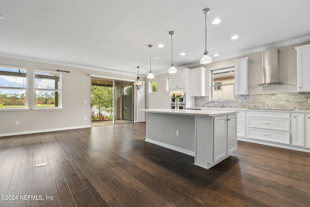 kitchen featuring white cabinetry, dark wood-type flooring, pendant lighting, wall chimney exhaust hood, and a center island