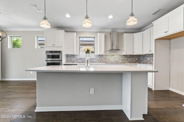 kitchen with wall chimney range hood, dark hardwood / wood-style flooring, white cabinetry, and a kitchen island