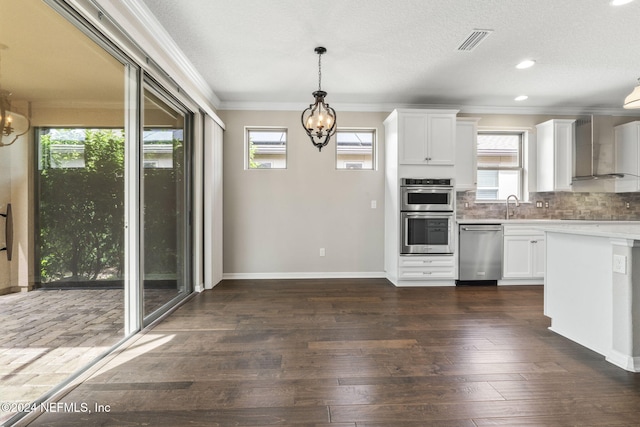 kitchen featuring appliances with stainless steel finishes, wall chimney range hood, white cabinetry, and a healthy amount of sunlight