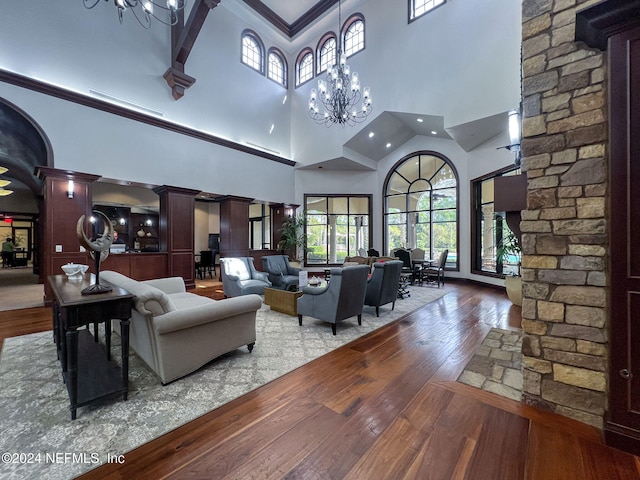 living room with high vaulted ceiling, wood-type flooring, ornate columns, crown molding, and a notable chandelier