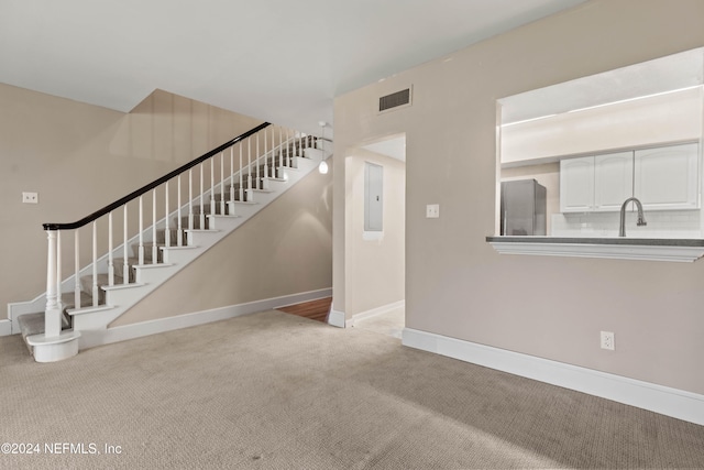 unfurnished living room with electric panel, light colored carpet, and sink