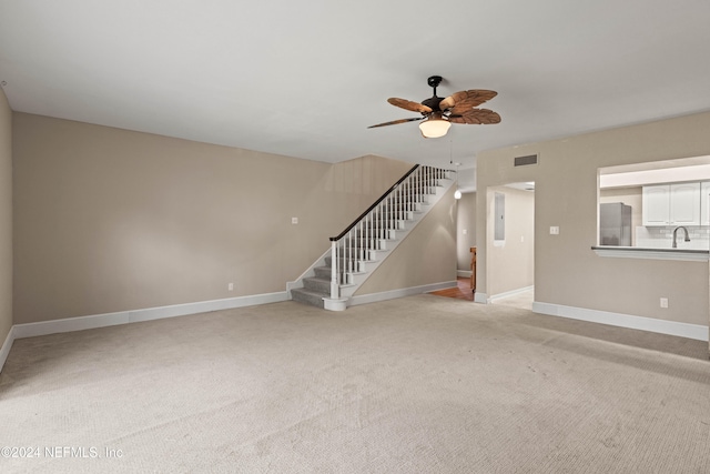 unfurnished living room with ceiling fan, sink, and light colored carpet