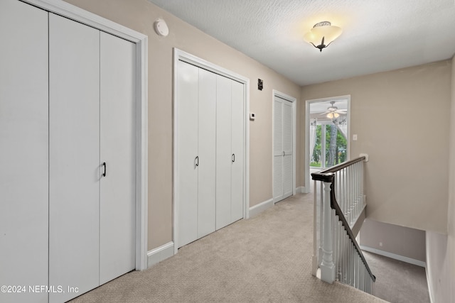 corridor featuring a textured ceiling and light colored carpet