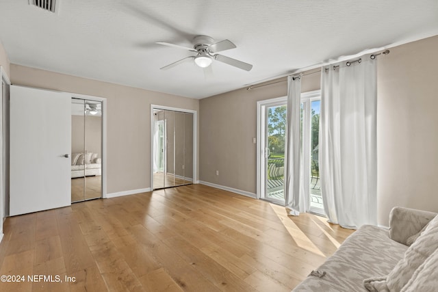 unfurnished bedroom featuring two closets, ceiling fan, a textured ceiling, access to exterior, and light hardwood / wood-style floors