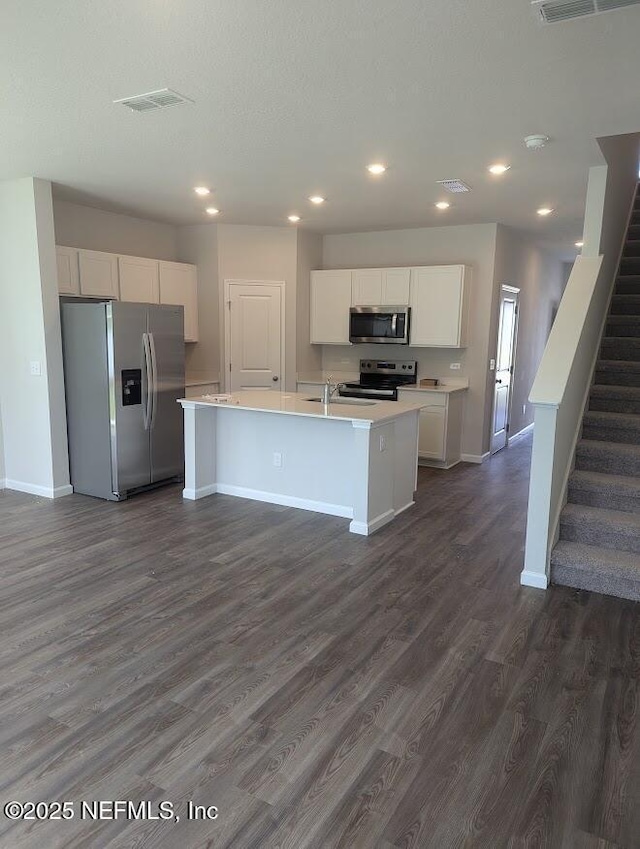 kitchen featuring a center island with sink, baseboards, appliances with stainless steel finishes, light countertops, and white cabinetry