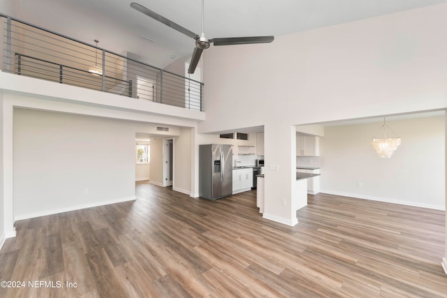 unfurnished living room with a towering ceiling, hardwood / wood-style flooring, and ceiling fan with notable chandelier