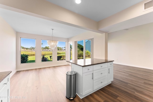 kitchen with white cabinets, hardwood / wood-style floors, a kitchen island, dark stone countertops, and decorative light fixtures