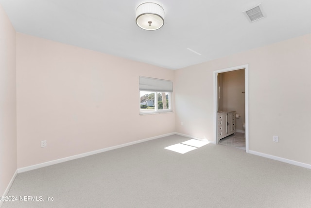 unfurnished bedroom featuring ensuite bath and light colored carpet