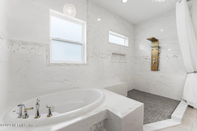 bathroom with independent shower and bath, tile patterned floors, tile walls, and a wealth of natural light