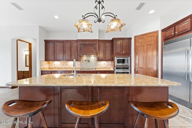 kitchen featuring tasteful backsplash, sink, an island with sink, hanging light fixtures, and built in appliances