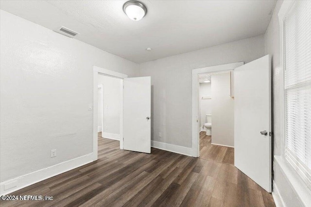 unfurnished bedroom featuring ensuite bathroom and dark hardwood / wood-style flooring