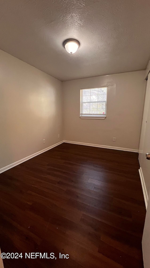 spare room with a textured ceiling and dark hardwood / wood-style flooring