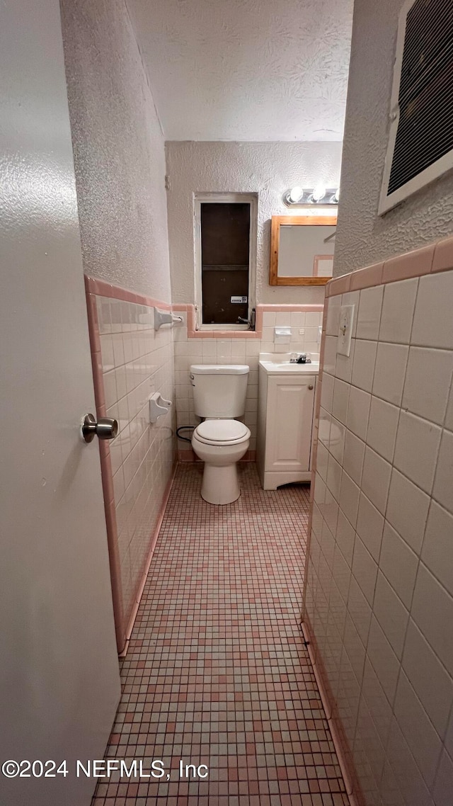 bathroom featuring tile patterned floors, toilet, tile walls, vanity, and a textured ceiling