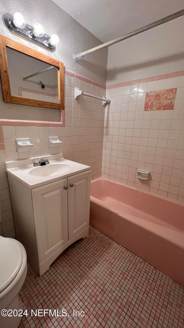 full bathroom with tile walls, vanity, tiled shower / bath combo, and toilet