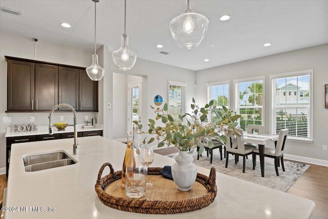 kitchen with light hardwood / wood-style floors, a textured ceiling, decorative light fixtures, and sink