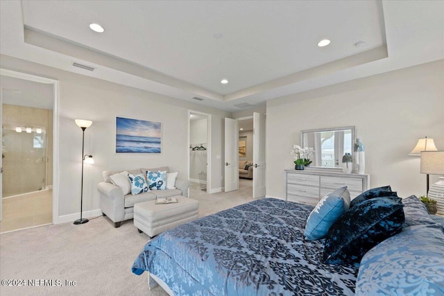 bedroom featuring light carpet, ensuite bathroom, and a tray ceiling