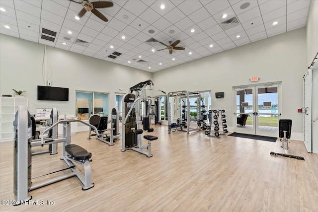 exercise room featuring light hardwood / wood-style flooring, ceiling fan, french doors, and a high ceiling